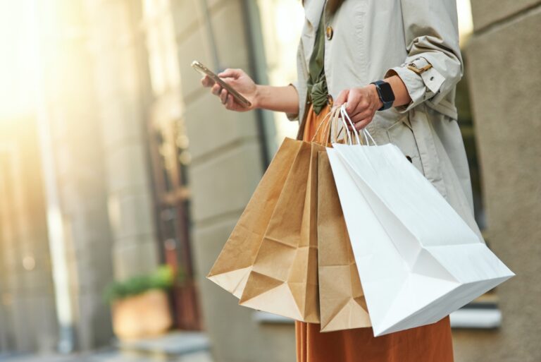 Texting sms to a friend. Cropped shot of a woman with shopping bags using her smartphone while standing on city street outdoors